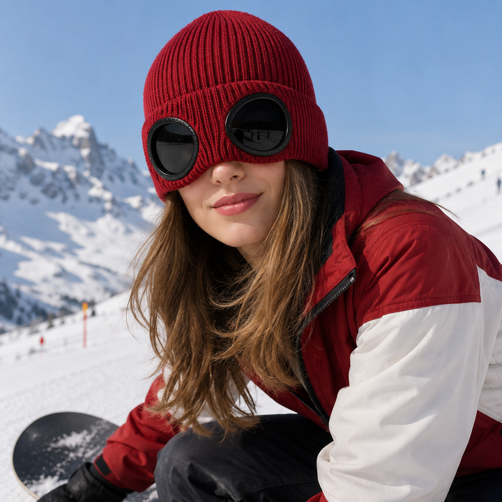 Woman wearing the goggle beanie in Red with the lenses down on a ski slope
