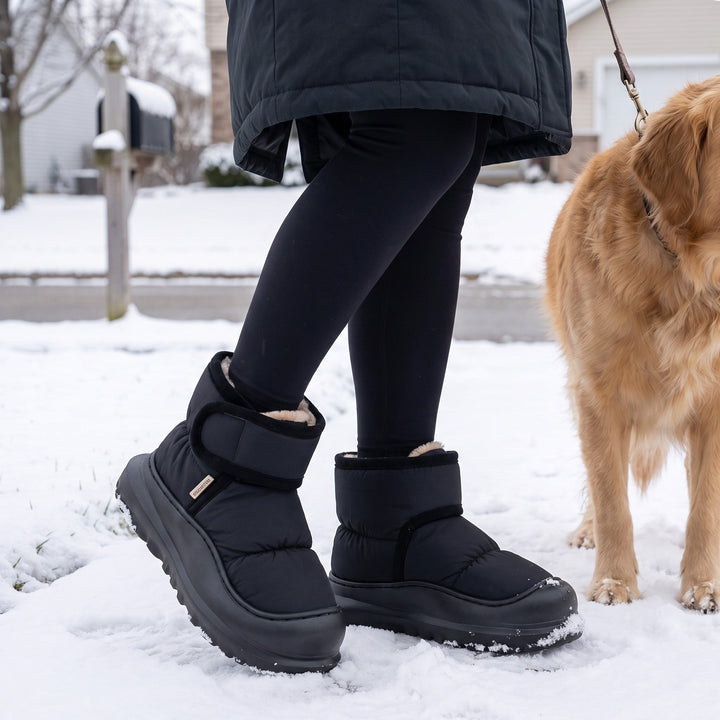 Woman walking a dog in the snow wearing black puffer slipper boots