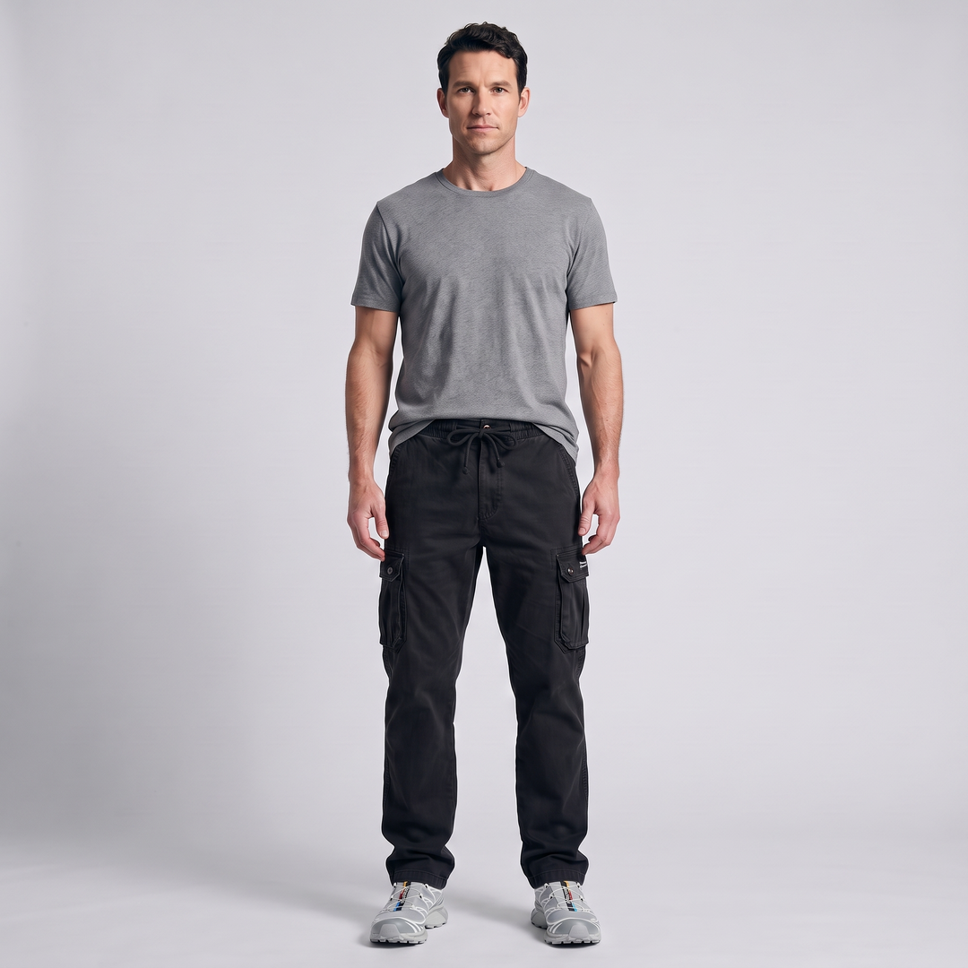 Man wearing black cotton cargo pants with the drawcord tied, grey t-shirt and trail shoes, full length front view
