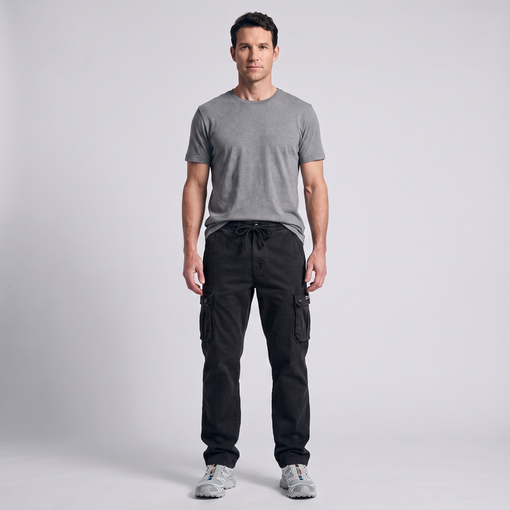 Man wearing black cotton cargo pants with the drawcord tied, grey t-shirt and trail shoes, full length front view