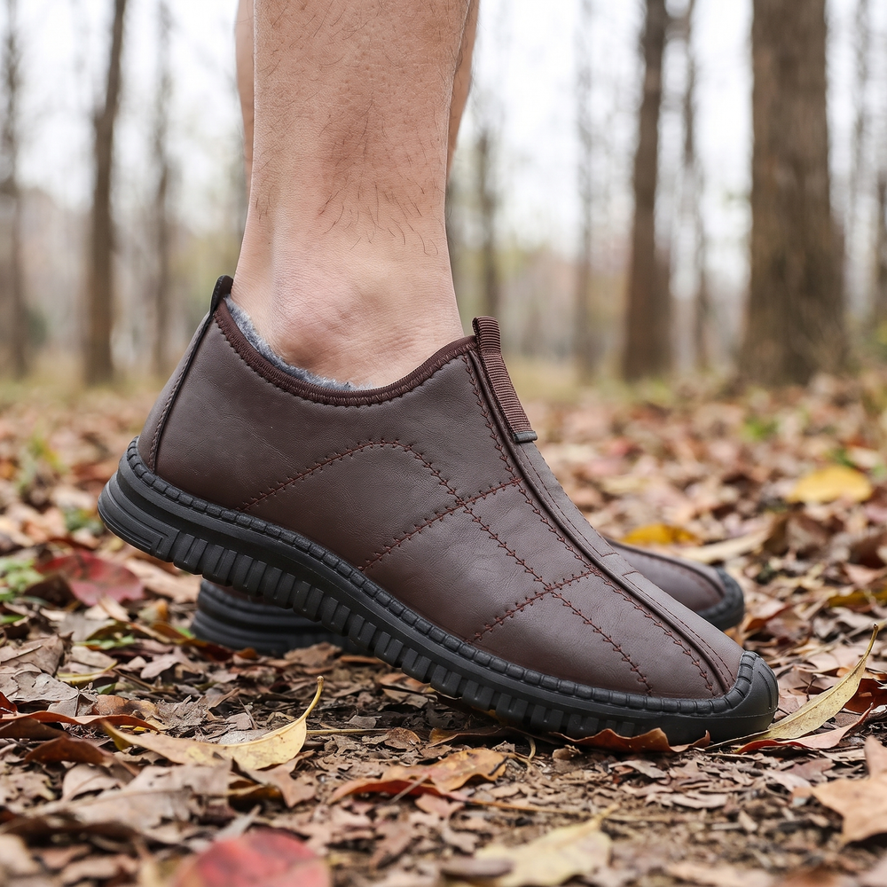 Man wearing brown slip on winter boots on a leafy forest path