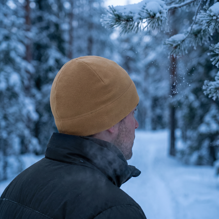 Man wearing the khaki fleece watch cap on a snowy forest trail