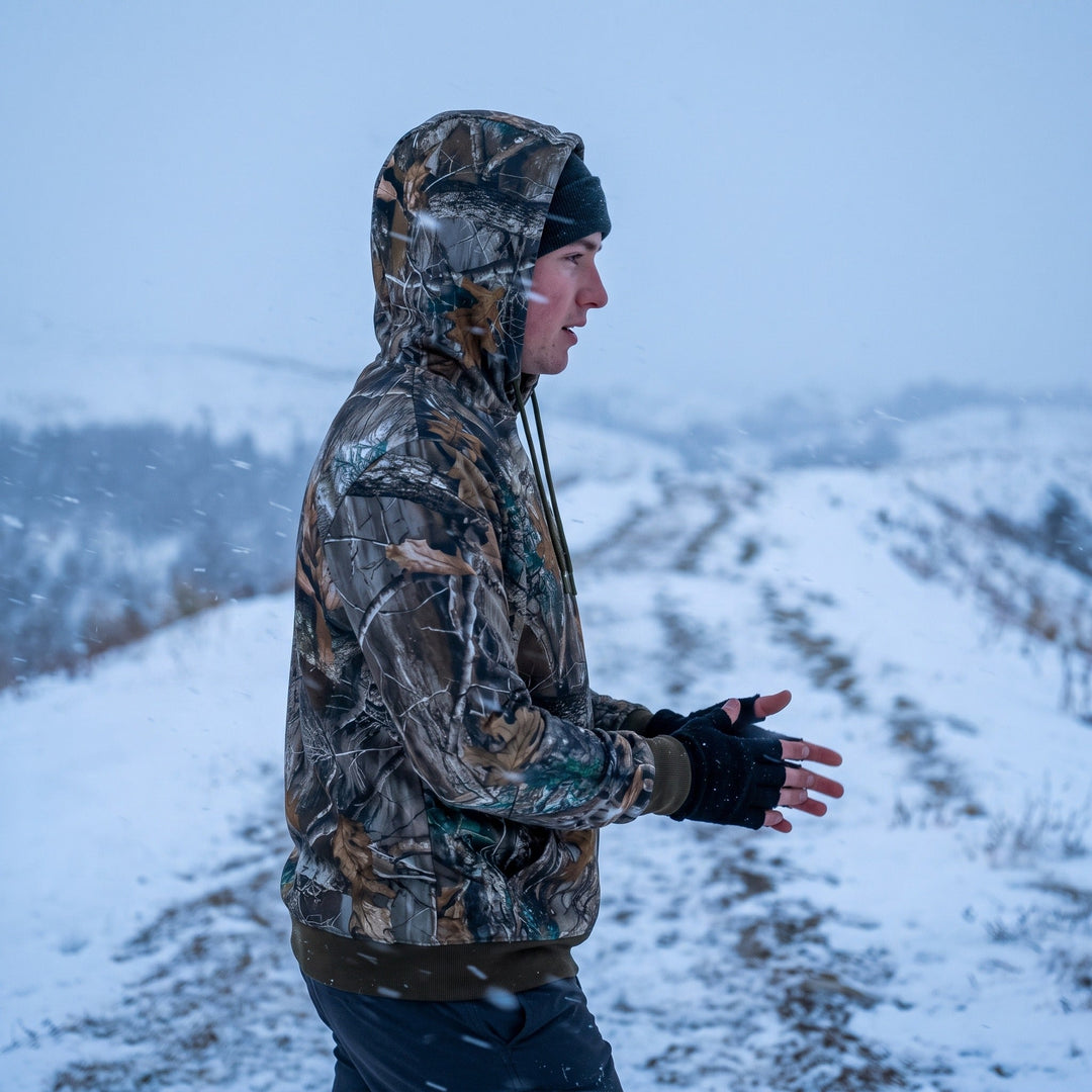 Man wearing the camo heated hoodie with the hood up on a snowy ridge