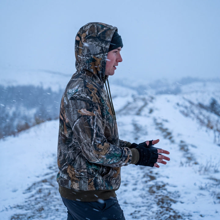Man wearing the camo heated hoodie with the hood up on a snowy ridge