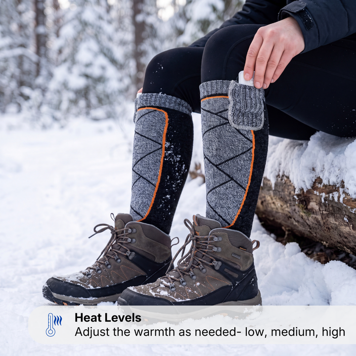 Woman in the snow putting a power bank into the cuff pocket of the heated ski socks