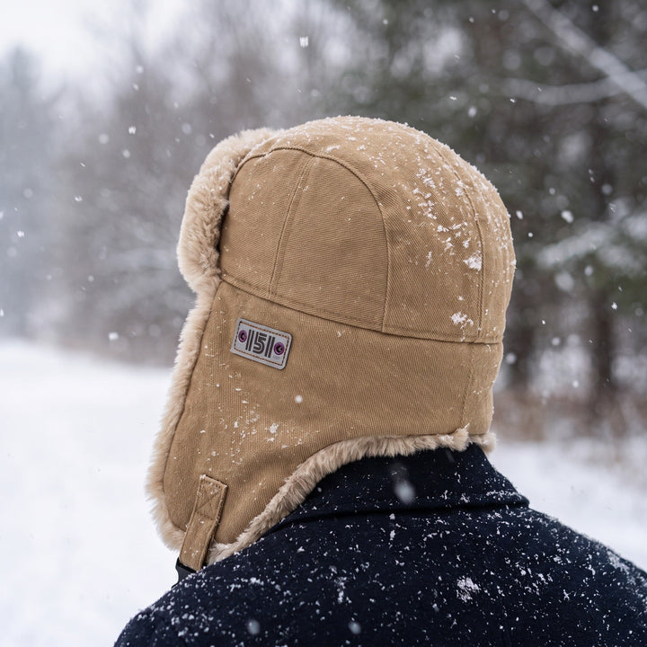 Man wearing the Khaki faux fur trapper hat with ear flaps in the snow