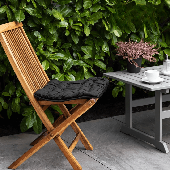 Black heated seat cushion on a wooden folding chair outdoors