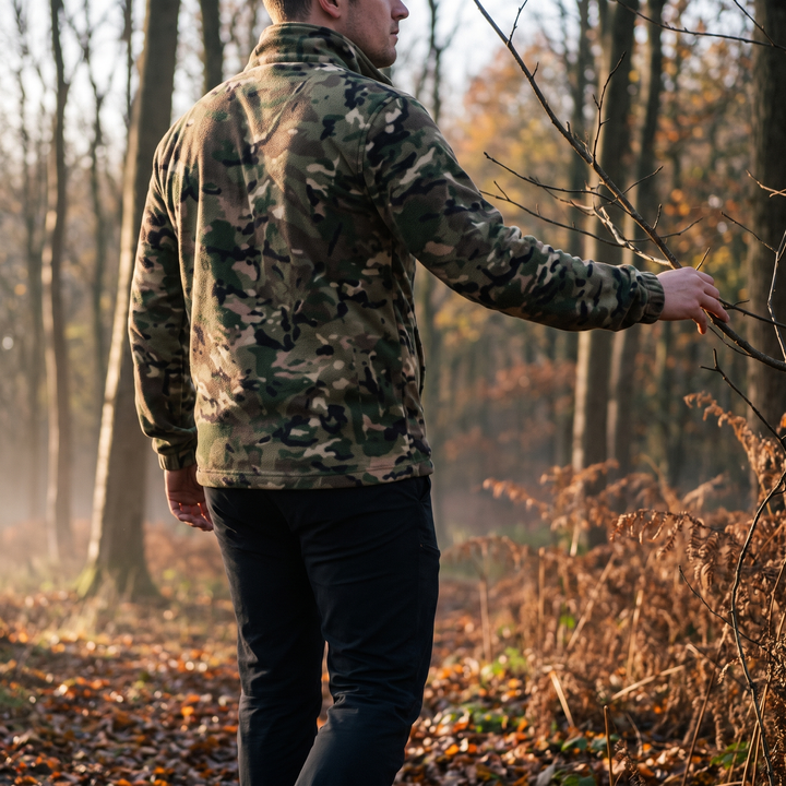 Man in camo fleece jacket moving quietly through autumn woodland at first light