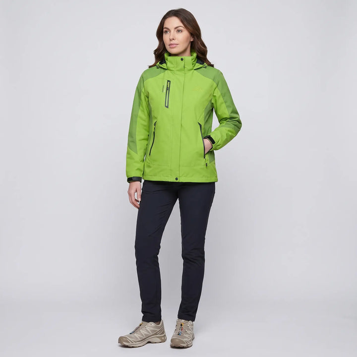Full-length view of a woman in the green insulated rain jacket with dark pants and trail shoes