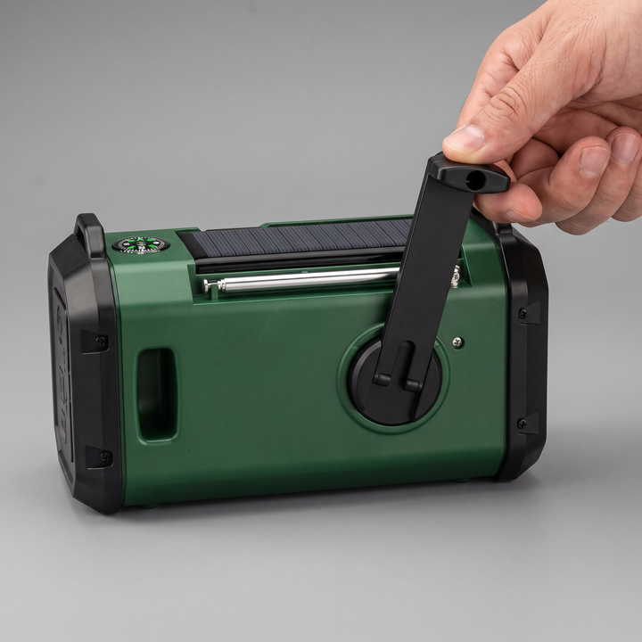 Hand turning the unfolded crank of the emergency weather radio, the empty slot it folds into visible beside it